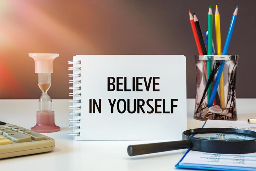 Believe in yourself is written on a notepad on an office desk with office accessories.