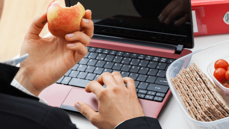 A businessman working at his computer while eating an apple