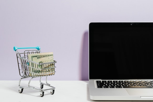 A shopping cart filled with cash beside a computer on a business desk
