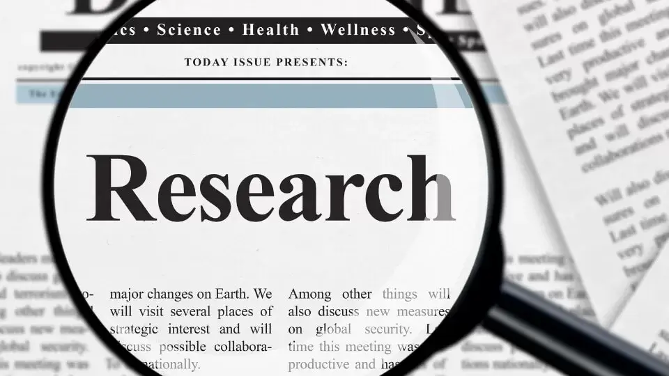 A magnifying glass focusing on the word research written on a newspaper